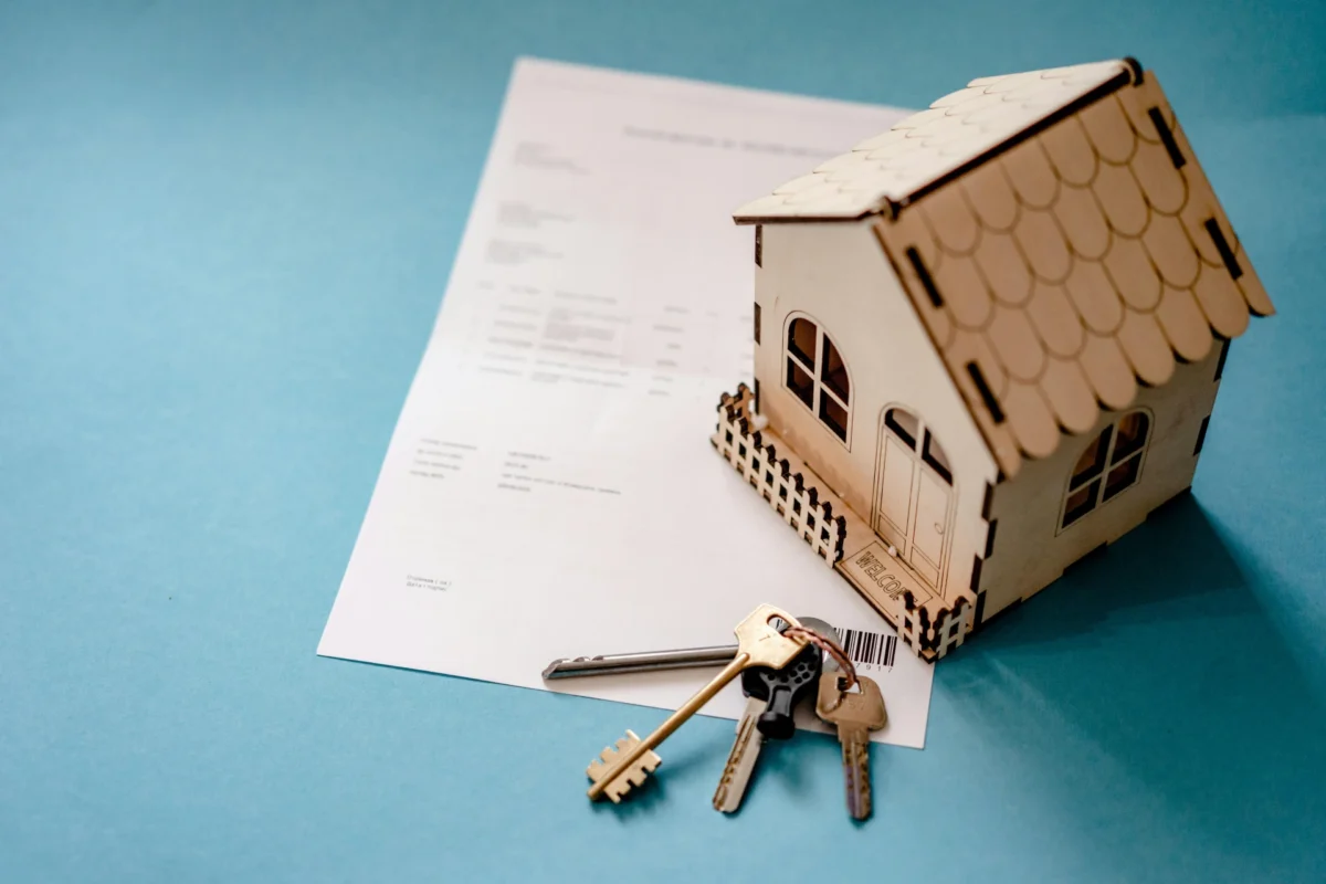 A wooden house model on a document with keys beside it.
