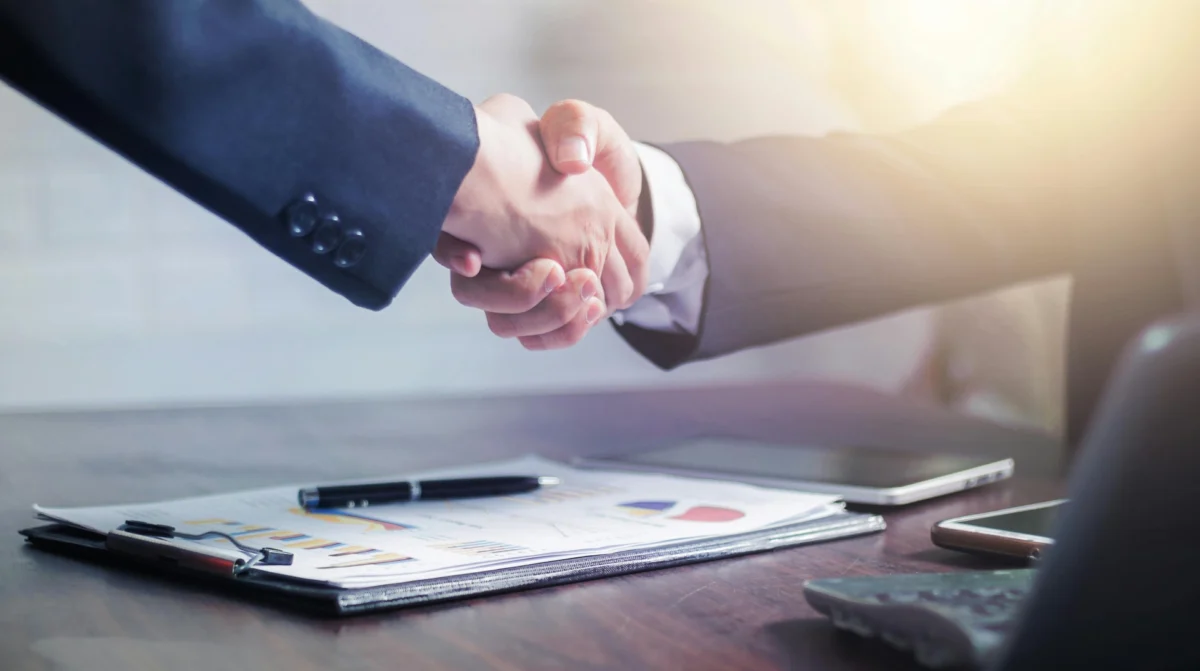 Two business professionals shaking hands over a contract.